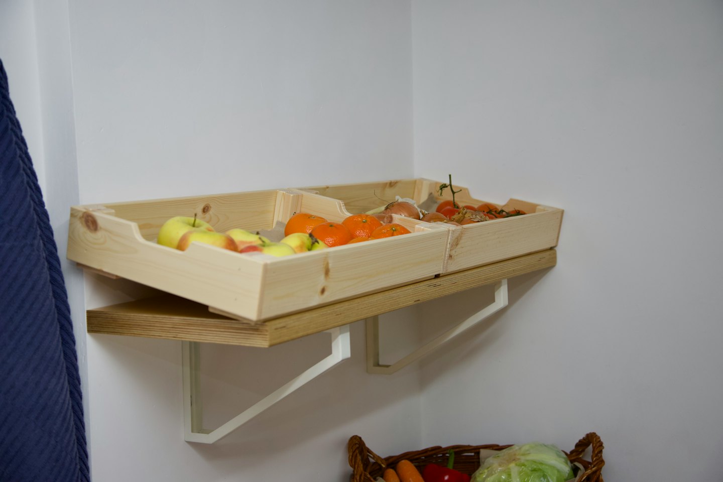 Holzkisten mit frischen Äpfeln, Mandarinen, Zwiebeln und Tomaten im Regal.